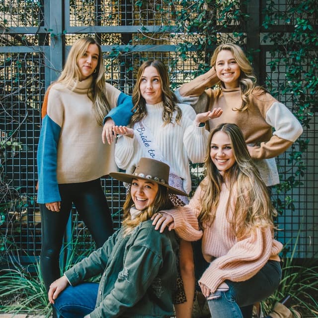 Five women posing together with smiles in casual attire.