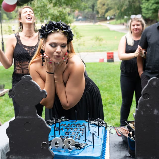 Person blowing out candles on a blue birthday cake at an outdoor party